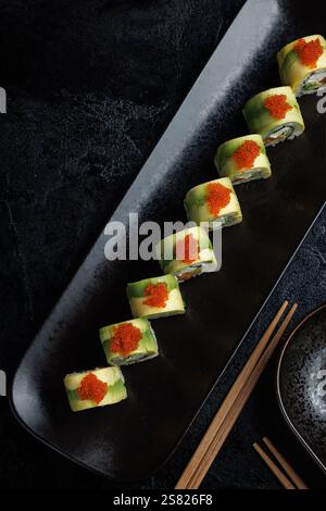 Un piatto di sushi ben presentato con uova di pesce arancione brillante. I panini sono ricoperti di avocado, ripieni di formaggio spalmabile, salmone, Foto Stock