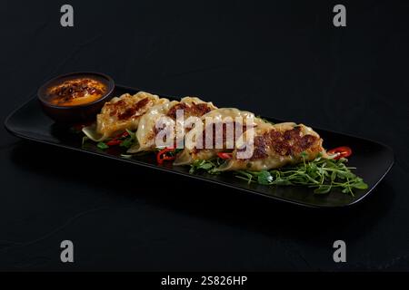 Gnocchi cotti al vapore e scottati con crosta dorata, serviti su un letto di verdure fresche e guarniti con fette di peperoncino rosso, abbinati a un sapone piccante Foto Stock