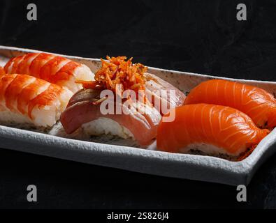 Un assortimento di sushi nigiri con gamberi, salmone e pesce scottato con verdure croccanti e grattugiate, presentato su un piatto rettangolare testurizzato Foto Stock