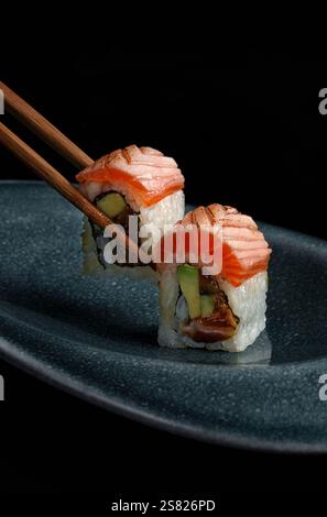Primo piano di due panini di sushi ripieni di avocado, salmone e altri ingredienti freschi, ricoperti di microgreen, presentati su sfondo nero per un'esperienza di Foto Stock