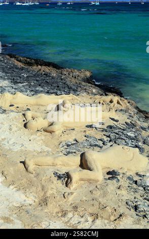 Sculture di sabbia di un uomo di famiglia donna cane bambino che prende il sole sulla spiaggia di Corralejo, Fuerteventura. Presa a dicembre 2024. Foto Stock