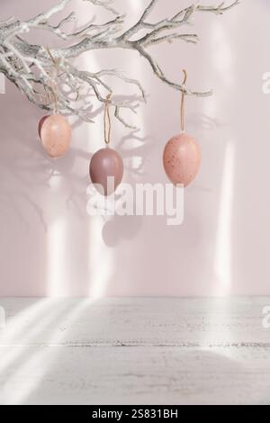 Uova di Pasqua appese al ramo su sfondo rosa pastello Foto Stock