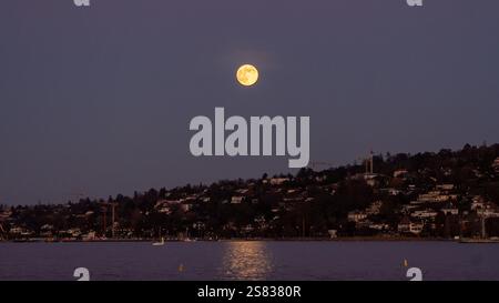 Una luna piena che si innalza all'orizzonte e riflette il suo bagliore sulle acque del lago di Ginevra, in Svizzera Foto Stock