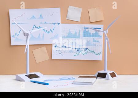 Diagrammi con note adesive vuote e modelli di turbine eoliche sul tavolo vicino alla parete beige. Concetto di energia verde Foto Stock