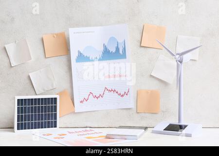 Diagrammi con note adesive vuote e modello di turbina eolica sul tavolo vicino alla parete luminosa. Concetto di energia verde Foto Stock
