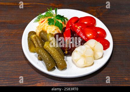 Un piatto mostra un vivace assortimento di verdure sottaceto, tra cui sottaceti verdi, peperoni rossi e aglio. Le erbe fresche aggiungono un tocco di verde, enhan Foto Stock