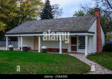 Una piccola casa bianca con un portico e un camino. La casa è circondata da un lussureggiante prato verde Foto Stock