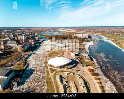 Prospettiva aerea di una città da un fiume parzialmente ghiacciato con ghiacci, caratterizzato da una struttura a cupola bianca, un ponte e un mix di moderno e storico Foto Stock