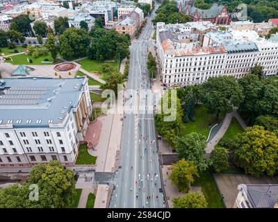 Ampia strada a riga, in Lettonia, fiancheggiata da edifici storici e da un parco con una fontana circolare, un paesaggio geometrico e facciate ornate. Foto Stock