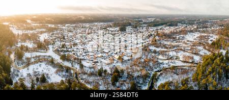 Città innevata circondata da un paesaggio boscoso, con fiumi tortuosi, campi aperti e luce del sole che emettono un caldo bagliore sulla scena invernale. Foto Stock