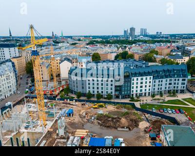 Cantiere con una gru gialla e strutture parzialmente costruite, circondato da edifici moderni e storici a riga, il paesaggio urbano della Lettonia. Foto Stock