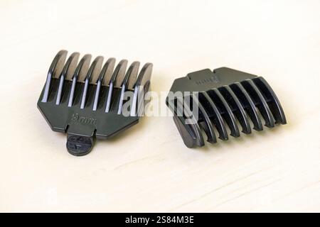 Su una superficie di legno chiaro sono disposte due protezioni nere del regolacapelli di varie lunghezze. Questi pettini guida sono strumenti essenziali per i parrucchieri, consentono Foto Stock