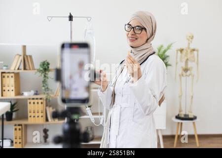Donna musulmana in hijab registra video che mostrano come usare contagocce medico. Medico donna mediorientale condivide le conoscenze mediche sulla registrazione. Educatore giovane, professionale e sicuro di sé in ambiente ospedaliero. Foto Stock