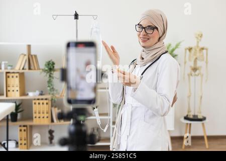 Donna musulmana in hijab registra video che mostrano come usare contagocce medico. Medico donna mediorientale condivide le conoscenze mediche sulla registrazione. Educatore giovane, professionale e sicuro di sé in ambiente ospedaliero. Foto Stock