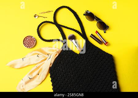 Composizione piatta con sacchetto per la spesa in macrame e prodotti per il trucco su sfondo giallo Foto Stock