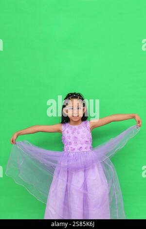 La bruna latina di 5 anni con occhiali e abito da principessa è felice e divertente a giocare durante la sua vacanza Foto Stock