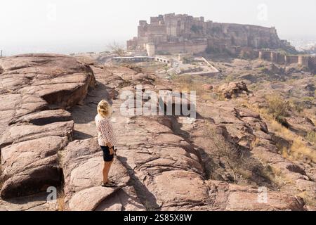Giovane donna bionda che gode della vista sul forte di Jodhpur mentre si trova sulla roccia nel Rajasthan, in India. Foto Stock