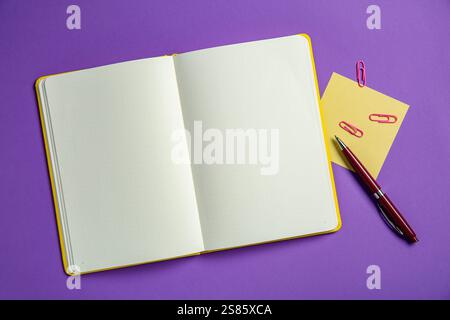 Blocco appunti vuoto, appunti, graffette e penna su sfondo viola, vista dall'alto. Spazio per il testo Foto Stock