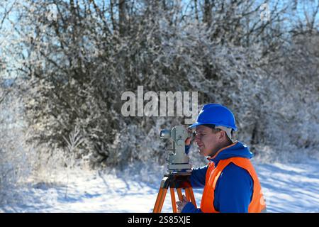 Surveyor che lavora con l'attrezzatura totale della stazione di teodolite in un paesaggio innevato durante l'inverno. Foto Stock