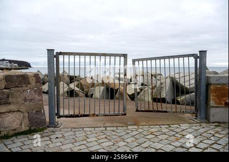 Vecchio cancello di metallo arrugginito aperto a metà su una scogliera rocciosa di fronte al mare Foto Stock
