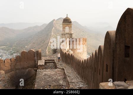 Giovane donna bionda che gode dell'alba sulla grande Muraglia di Jaipur nel Rajasthan, India. Luce mattutina sulle montagne nebbiose e sulle mura di fortificazione Foto Stock