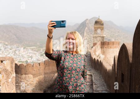 Giovane donna bionda che si fa selfie sulla grande parete di Jaipur nel Rajasthan. Felice sorridente turista europeo che esplora l'India. Foto Stock