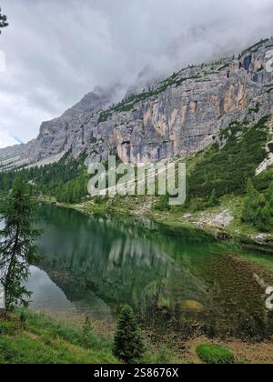 Lago tranquillo circondato da alberi lussureggianti e ripide montagne rocciose, Croda di Lago, Dolomiti, Italia. Riflessi in acque calme, ambiente sereno Foto Stock