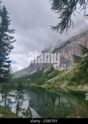 Lago tranquillo circondato da alberi lussureggianti e ripide montagne rocciose, Croda di Lago, Dolomiti, Italia. Riflessi in acque calme, ambiente sereno Foto Stock