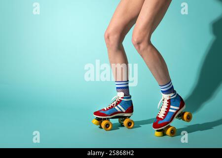 Donna che indossa pattini vintage, calze a rete e pantaloncini corti in posa su sfondo turchese Foto Stock