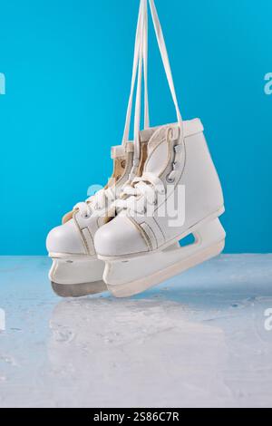 Pattini di ghiaccio bianchi appesi a lacci su un vivace sfondo blu, che mettono in risalto le attività invernali creative e la gioia stagionale. Foto Stock
