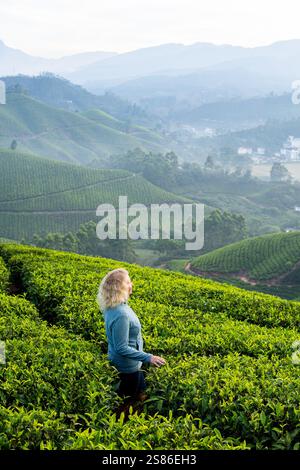 Giovane donna bionda che fa trekking tra le piantagioni di tè a Munnar. Turismo ecologico in Kerala, India Foto Stock