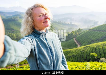 Giovane donna sorridente che si fa selfie con piantagioni di tè a Munnar. Turismo ecologico in Kerala, India Foto Stock