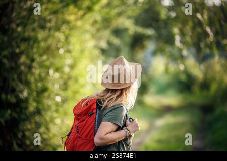 Una donna escursionistica con cappello e zaino rosso cammina lungo il sentiero di trekking nella foresta Foto Stock
