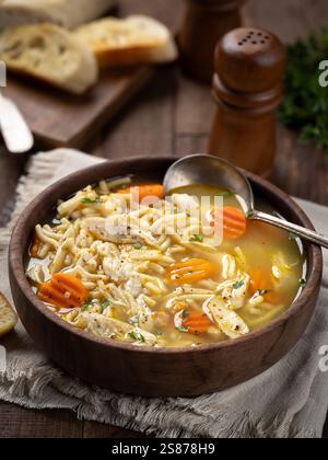 Ciotola di zuppa di spaghetti di pollo con carote su un tovagliolo e fette di baguette su un tavolo di legno Foto Stock