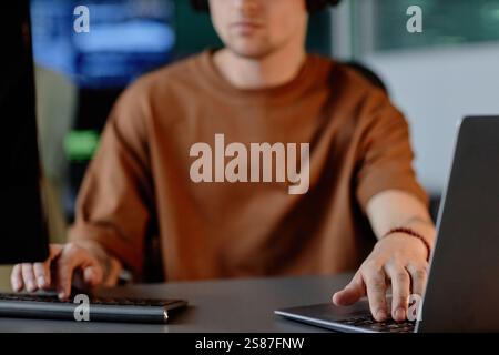 Immagine ritagliata di un programmatore maschio irriconoscibile che utilizza la codifica di computer e laptop su più schermi mentre lavora nell'ufficio dell'azienda IT, spazio di copia Foto Stock