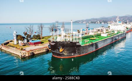 Nave cisterna GPL ancorata al terminal industriale per il carico o lo scarico di gas in condizioni di sole, catturata dalla vista aerea. Industria marittima moderna con condutture e riflessione dell'acqua. Foto Stock