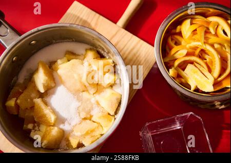 Una ricetta preparata con mele a dadini e bucce di agrumi poste in pentole su un piano di lavoro della cucina. Foto Stock