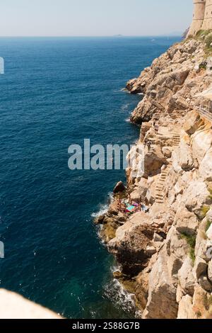 Guardando a ovest dalle mura meridionali della città, costruite lungo alte scogliere di roccia difensive, presso i bagnanti e i bagnanti che spesso saltano nel blu del mare Adriatico, sotto la città vecchia fortificata di Dubrovnik. Croazia. (138) Foto Stock