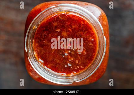 Vaso in vetro con verdure fresche tritate in scatola, lecho su sfondo nero. Cibo in scatola fatto in casa. Salsa naturale fatta in casa di pomodori rossi e peperoni. Inizio vi Foto Stock
