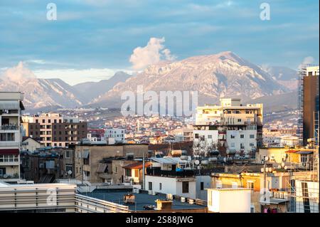 Vista dall'alto su edifici di appartamenti colorati e montagne al crepuscolo nella città di Tirana, Albania, 12 dicembre 2024 Foto Stock