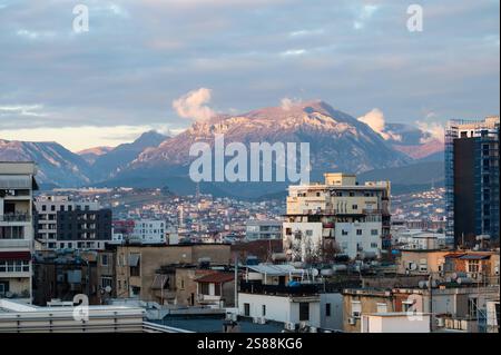 Vista dall'alto su edifici di appartamenti colorati e montagne al crepuscolo nella città di Tirana, Albania, 12 dicembre 2024 Foto Stock