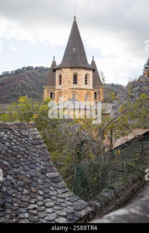 L'iconico campanile della chiesa abbaziale di Sainte-Foy, visto attraverso i tetti rustici nel villaggio medievale di Conques, Aveyron, Francia Foto Stock