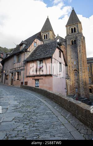 Una tortuosa strada acciottolata nel villaggio medievale di Conques, Aveyron, Francia, che conduce alla Chiesa abbaziale di Sainte-Foy Foto Stock
