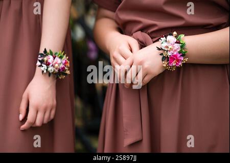 Primo piano di due donne con abiti in malva che indossano delicati corsaggi floreali da polso. I fiori sono rosa, bianco e oro, aggiungendo un tocco di eleganza. Foto Stock