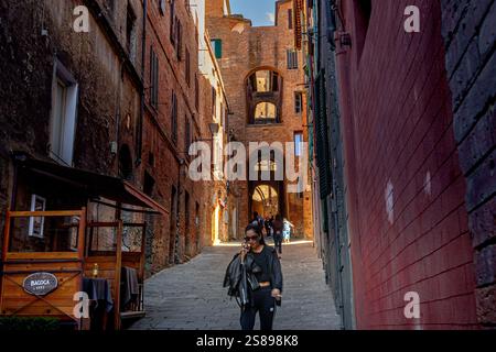 Una donna che cammina lungo la ripida strada stretta di via della Galluzza , una ripida strada stretta con archi medievali a Siena, Italia Foto Stock