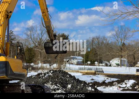 Un escavatore funziona in un ambiente innevato, spostando la terra vicino a case sotto l'area di fondazione dei lavori Foto Stock