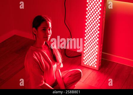 Primo piano di una giovane donna durante una sessione di terapia a luce rossa all'interno Foto Stock