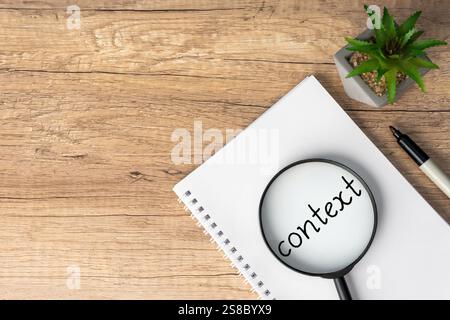 Una lente d'ingrandimento è posizionata sopra la parola "contesto" scritta su un notebook, sottolineando l'importanza della comprensione del contesto. Foto Stock