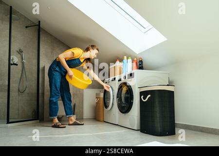 Lavatrice a carico di donna nella moderna e minimalista lavanderia interna Foto Stock