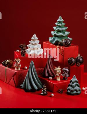 Sfondo natalizio con scatole regalo e colorate figure di cioccolato con alberi di Natale, orsi e palle. Sfondo rosso Foto Stock